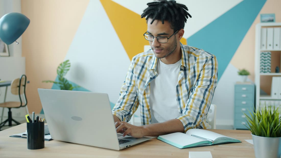 A young man working at a laptop against a colourful wall